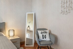 A bedroom with a bed, a nightstand, a lamp, a chair with a pillow, a mirror, and a wall with a dreamcatcher. - Apartment 'Ferienwohnung Seus' with Wi-Fi (Dorfprozelten)