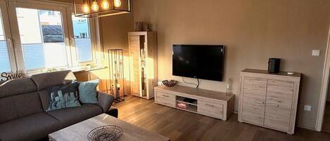 A living room with a sofa, coffee table, TV, cabinet, and a tall floor lamp.