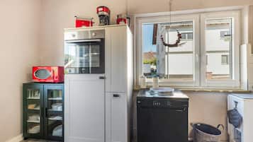 A compact kitchen with a white refrigerator, a black dishwasher, and a red vintage radio.
