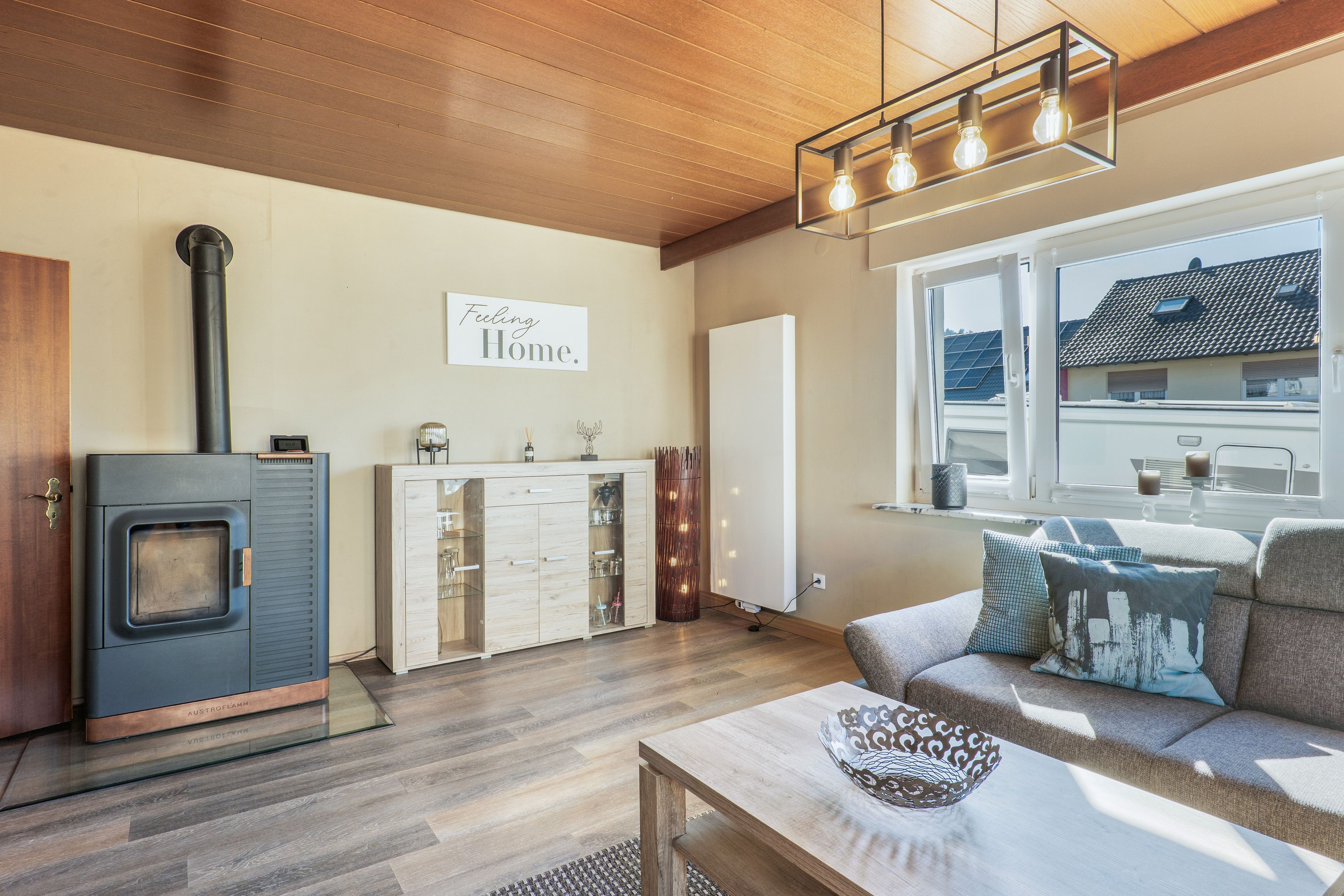 Ein modernes Wohnzimmer mit Kaminofen, einer Couch mit gemusterten Kissen und einem Schild mit der Aufschrift 'Feeling Home'.