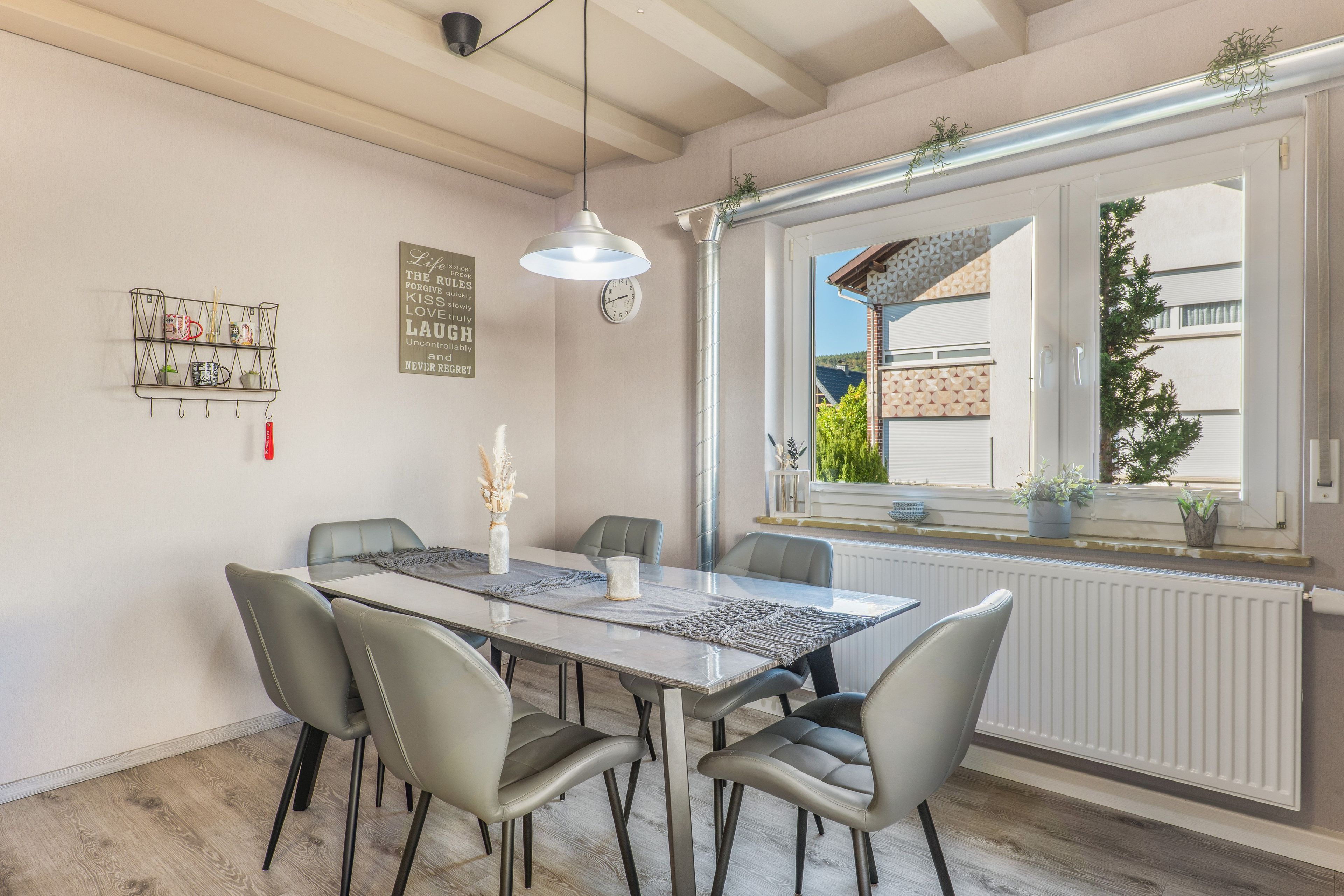 A dining area with a table, chairs, a hanging light, and a window with plants.
