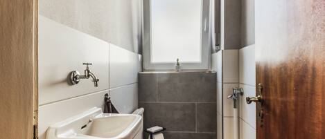 A compact bathroom with a sink, toilet, and a small window above the shower.