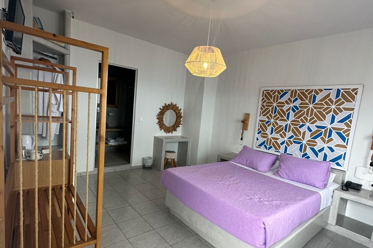 A bedroom with a bed, a hanging light fixture, a mirror, a wall art piece, and a wooden chair.