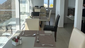Un moderno comedor con vistas a un paisaje montañoso. Se observan mesas y sillas dispuestas para comer, con una estación de buffet visible al fondo.