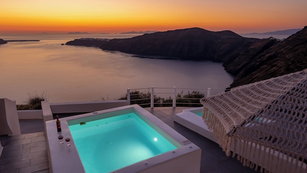 Una piscina con vista al atardecer, una botella de vino y una silla.