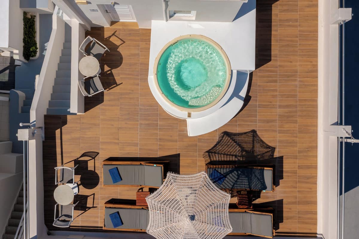 A rooftop pool area with a circular hot tub, sun loungers, and a large umbrella.