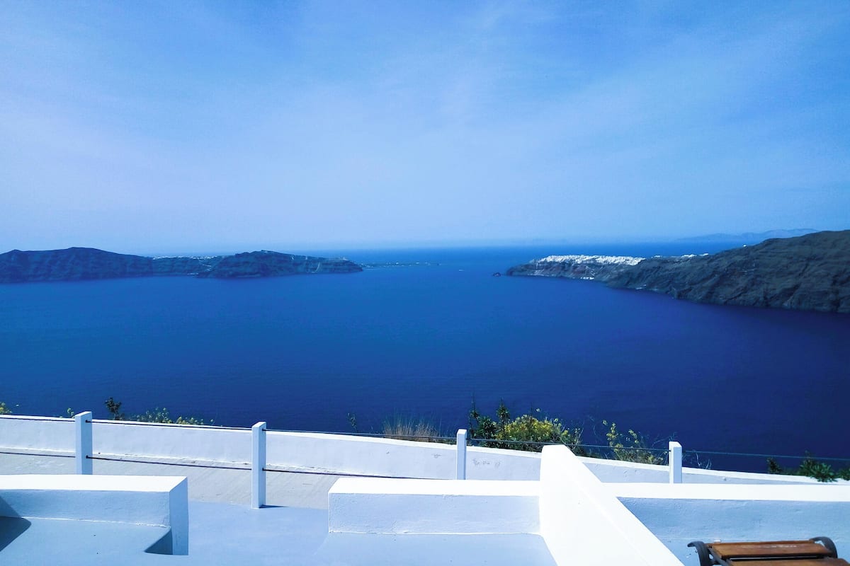 A coastal view with a clear blue sky, a calm sea, and rocky terrain.