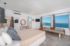 Un dormitorio moderno con una cama grande, una zona de estar, un televisor y vistas al mar.