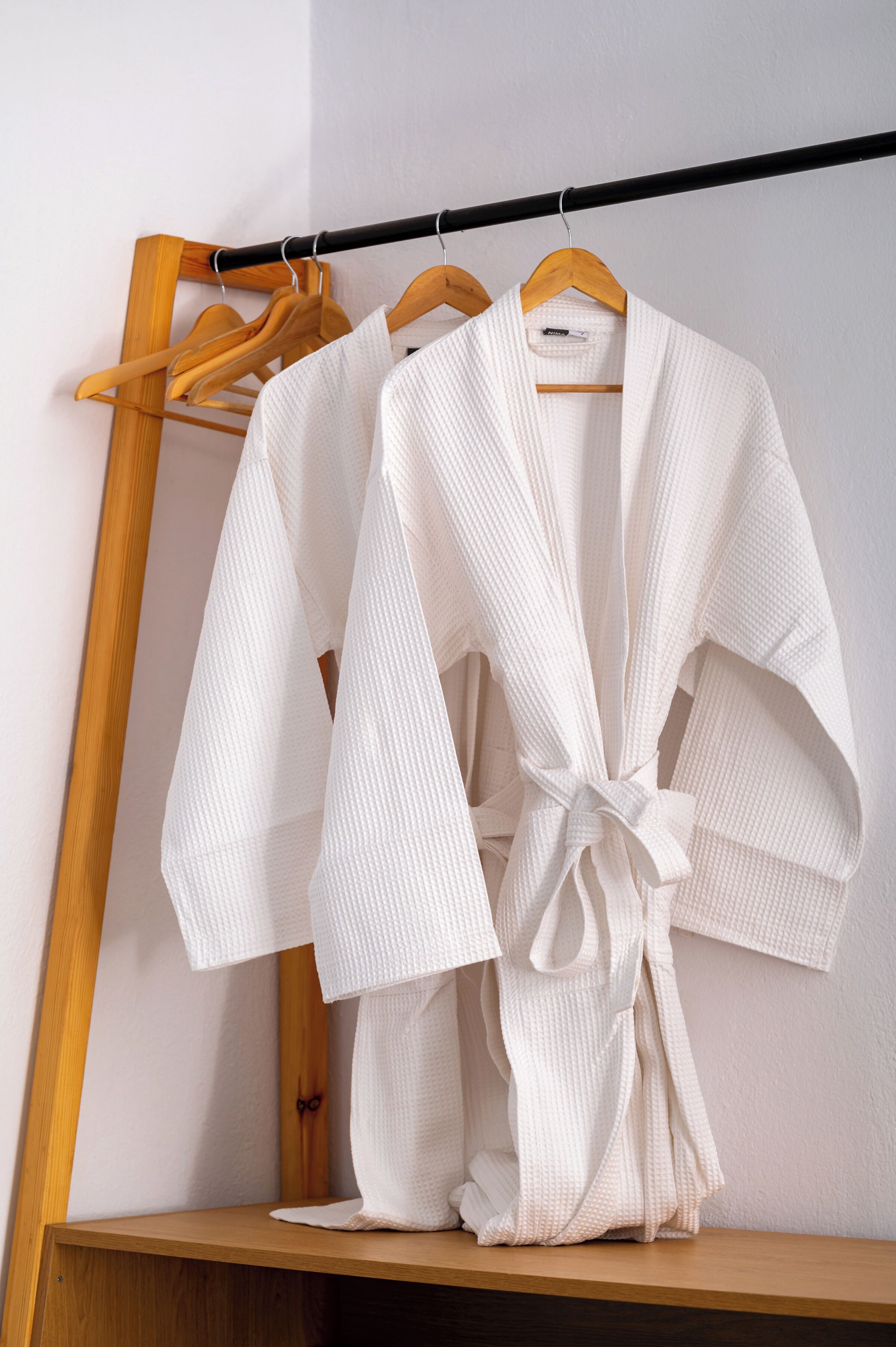 Une robe blanche est suspendue à un cintre en bois, appuyée contre un mur.