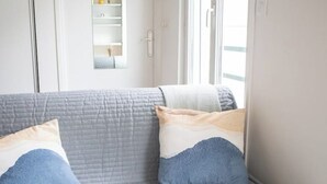 A room with a grey sofa, two pillows, and a window. - Cosy studio in the heart of Bastille - Peace, comfort and Parisian spirit (Paris)