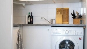 A compact kitchen with white cabinets, a washing machine, a wooden cutting board, and a knife block. - Cosy studio in the heart of Bastille - Peace, comfort and Parisian spirit (Paris)
