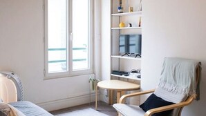 A room with a bed, a chair, a small table, and a shelf with a TV and some items. - Cosy studio in the heart of Bastille - Peace, comfort and Parisian spirit (Paris)