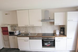 Una cocina moderna con armarios blancos, microondas, fregadero, estufa y cafetera.