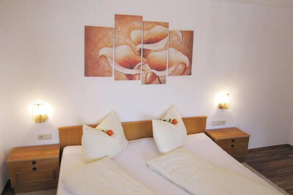 Una habitación de hotel con una cama, dos mesitas de noche, una lámpara de pared y un cuadro.