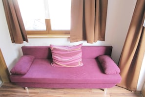 A purple sofa with a decorative pillow in front of a window with brown curtains. - Apartment in Kappl including Silvretta Card (Kappl)