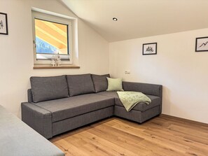 En moderne stue med en grå hjørnesofa, et vindue med udsigt til et bjerg og trægulv.