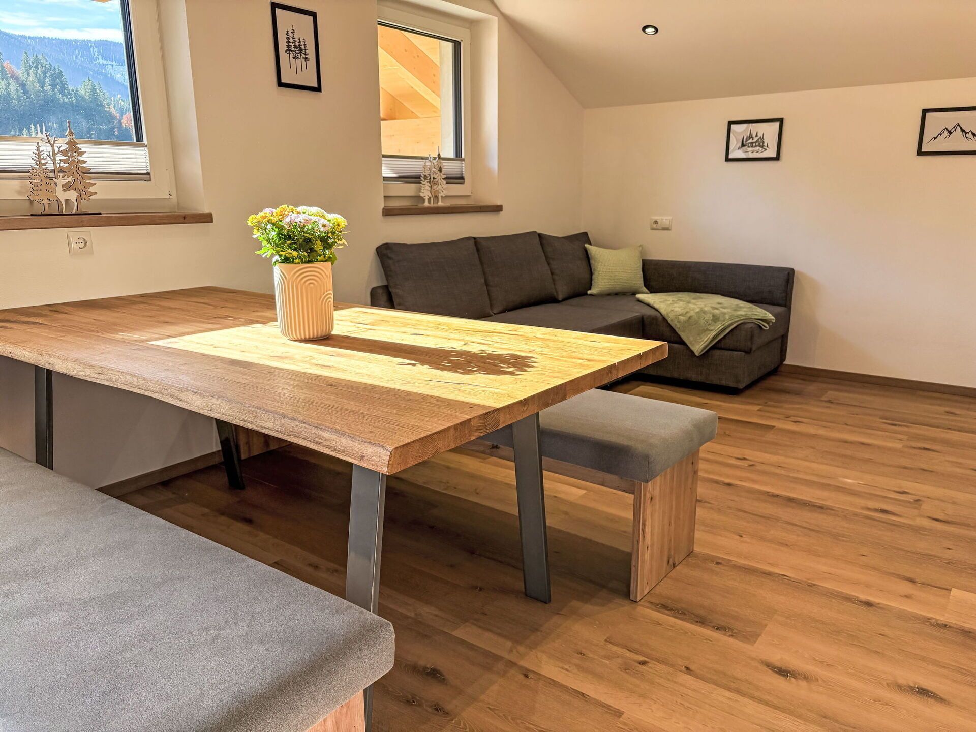 Un soggiorno moderno con un tavolo da pranzo in legno, un divano grigio e vista all'esterno tramite un'ampia finestra.