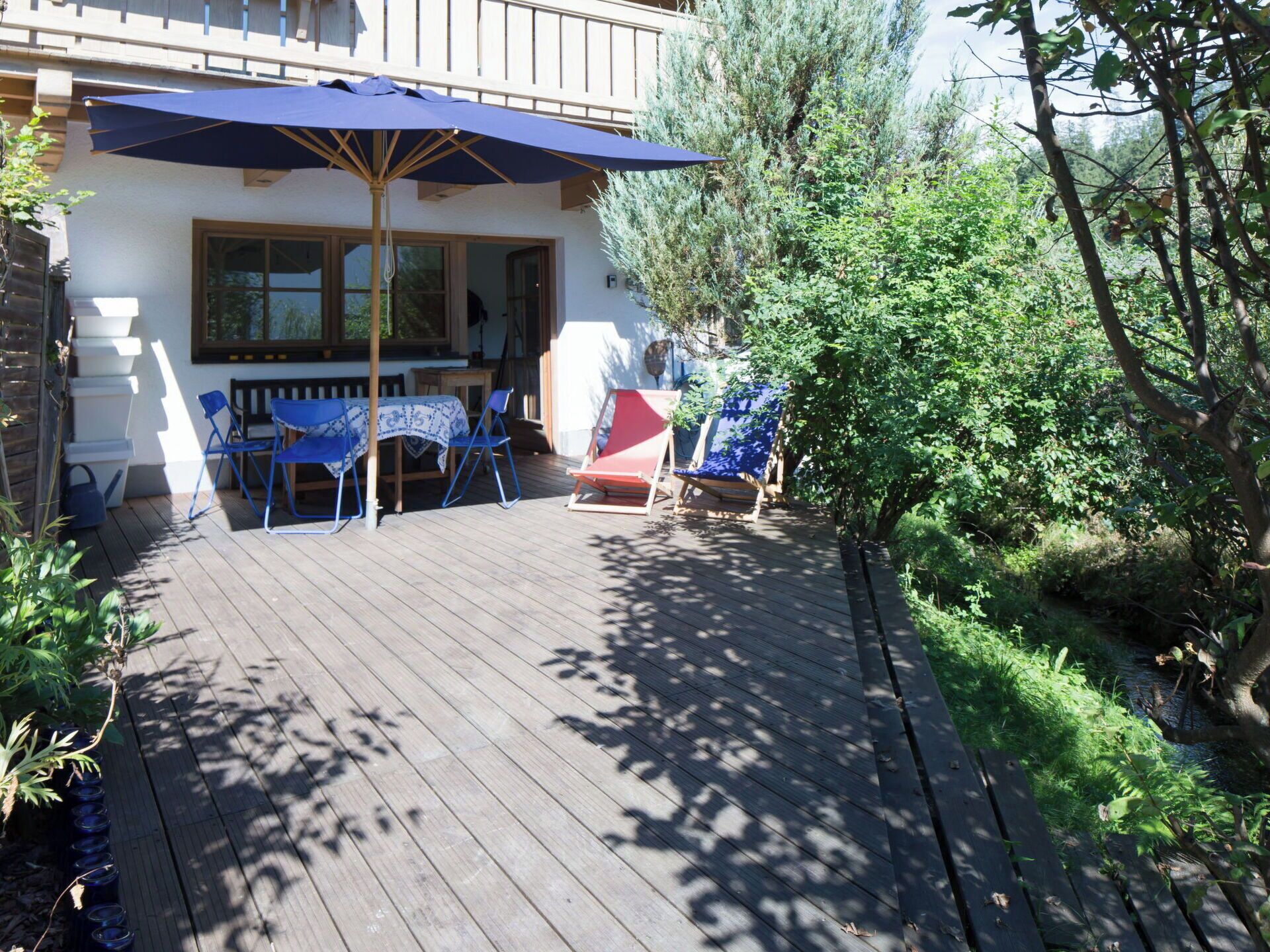A wooden deck with a table and chairs, an umbrella, and a bench.