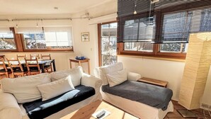 Ein gemütliches Wohnzimmer mit einer Couch, einem Couchtisch und einem Fernseher. Es gibt einen Essbereich mit Tisch und Stühlen.