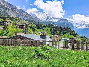 Eine gebirgige Landschaft mit Holzzaun, grünen Feldern und Gebäuden mit geneigten Dächern.