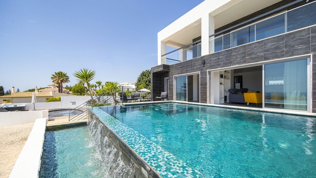 Ein moderner Poolbereich mit klarem, blauem Pool, einer Sonnenterrasse und einem zeitgemäßen Gebäude mit großen Fenstern.