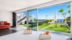 Une chambre d’hôtel moderne dotée d’une grande porte-fenêtre coulissante donnant sur un espace extérieur privé avec une piscine, des chaises longues et une vue sur l’océan.