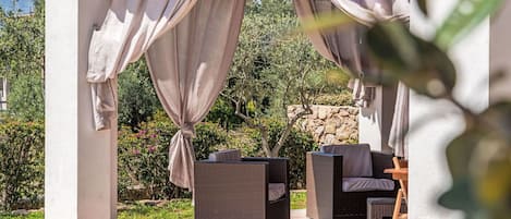 A covered outdoor seating area with wicker furniture and beige curtains.