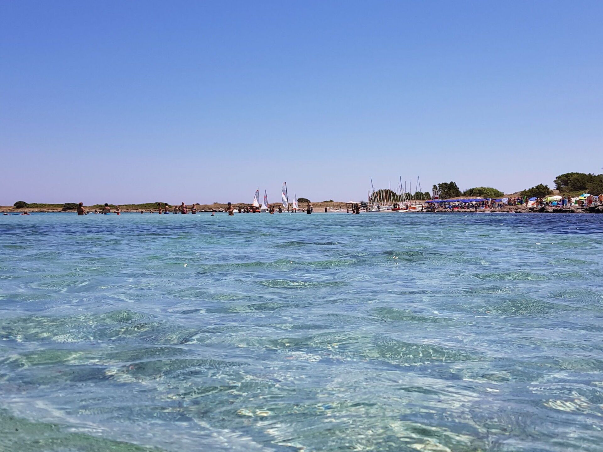 A beach scene with clear water, boats, and people.