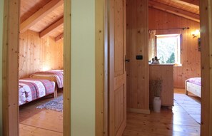 A wooden cabin with two beds, a small window with a view, and a door leading to another room.