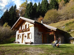 A stone house with a wooden balcony, a stone fireplace, and a small porch area with outdoor seating.