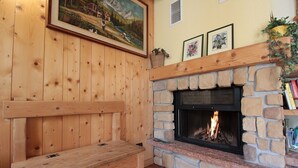 Ein gemütliches Zimmer mit Kamin aus Stein, einer Holzbank und einem Gemälde an der Wand.