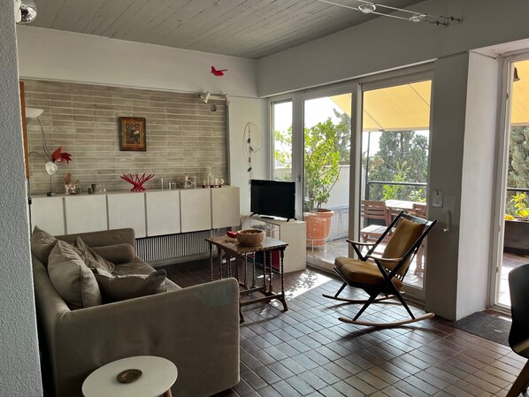 A modern living room with a sofa, a small table, a TV, and a balcony with a chair. - Luminous duplex apt in Plaka, Acropolis views (Athina)