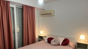 Un dormitorio con una cama, dos mesitas de noche con lámparas, una ventana con cortinas y un equipo de aire acondicionado en la pared.