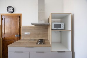A kitchen with a microwave, wooden cabinets, a stove, and a clock on the wall. - Cozy Apartment Place Paoli – Mountain View, Heart of Corte (Corte)