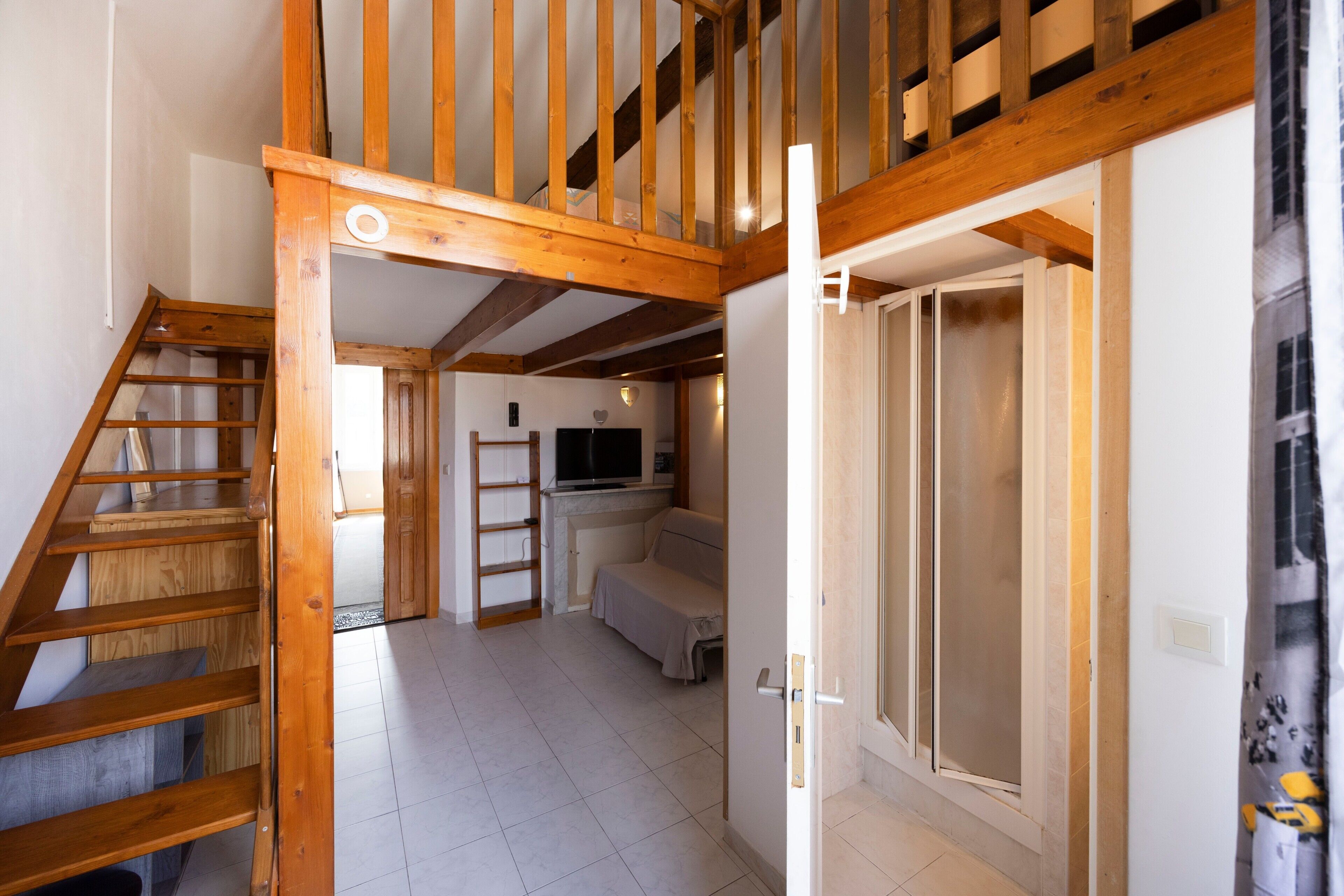 Amplia habitación con una escalera de madera, un sofá y un televisor.