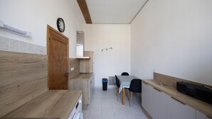 Cocina compacta con encimeras de madera, lavadora integrada, mesa de comedor con sillas y un reloj fijado a la pared.