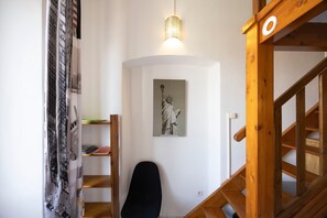 A room with a wooden staircase, a black chair, a wall-mounted light fixture, and a framed picture of a statue.