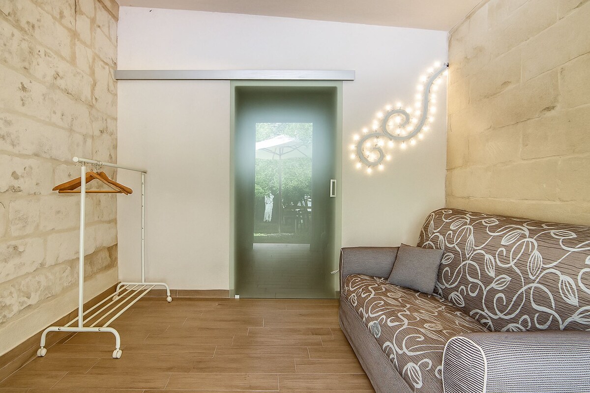 A room with a wooden floor, a patterned sofa, a white hanging rack, and a door leading to an outdoor area.