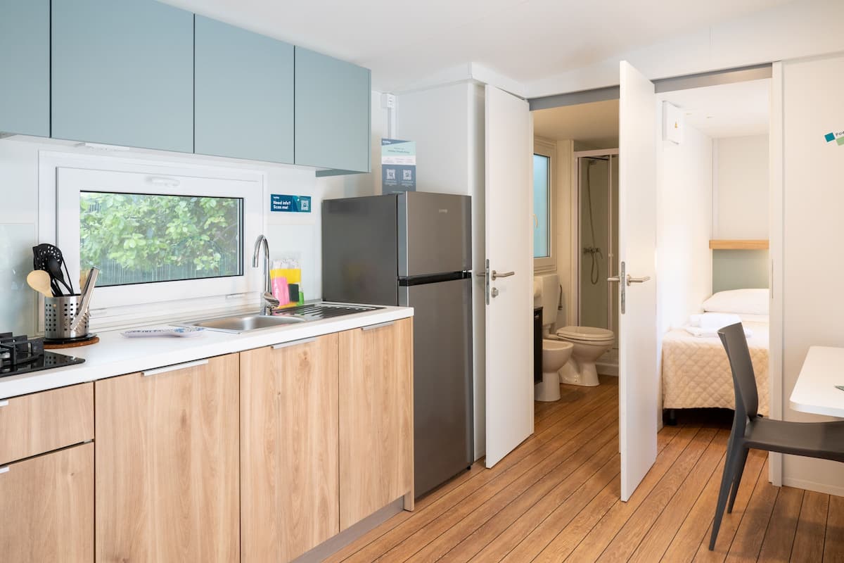 A compact kitchen with a microwave, refrigerator, and sink. A wooden cabinet and a window are also visible.