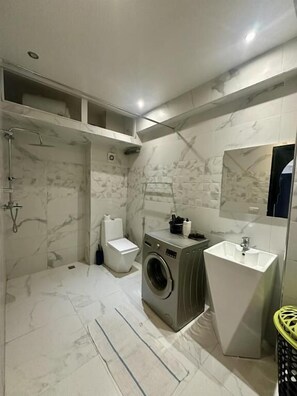 A modern bathroom with a marble floor, a built-in washing machine, a pedestal sink, and a shower enclosure. - studio équipé et centrale -Guéliz (Marrakech)