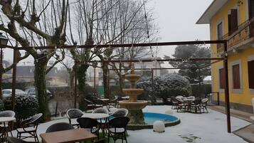 Un patio con mesas al aire libre, una fuente central y un edificio amarillo al fondo.