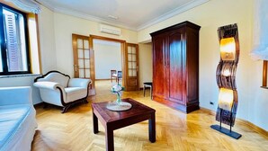 A room with a wooden herringbone floor, a white sofa, a wooden cabinet, and a modern floor lamp. - Room 'Suite Presidencial' with Shared Terrace, Wi-Fi and Air Conditioning (Guadarrama)