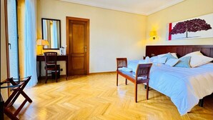 A hotel room with a bed, a desk, a chair, a door, and a painting on the wall. - Room 'Suite Presidencial' with Shared Terrace, Wi-Fi and Air Conditioning (Guadarrama)