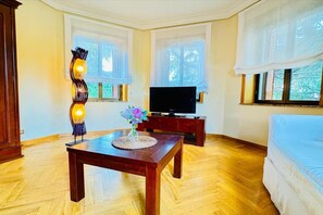 Ein Zimmer mit Holzboden, einem Fernseher auf einem Schrank, einem Tisch mit Blumen und einem Bett.