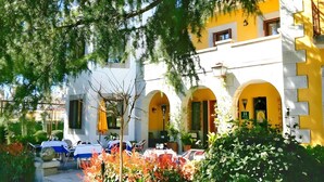Un edificio con paredes amarillas y blancas, arcos y mobiliario exterior con mesas y sillas.