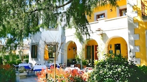A building with yellow and white walls, arched doorways, and outdoor seating with tables and chairs.