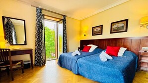 Habitación de hotel con dos camas, un escritorio, una silla, un espejo grande y un ventanal corredizo al exterior.