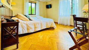 A room with a bed, a desk with a telephone, a chair, a television on the wall, and a window with curtains. - Room 'Habitación Doble' with Balcony, Wi-Fi and Air Conditioning (Guadarrama)