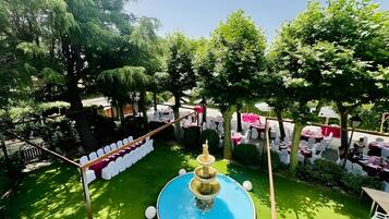 A pool with a fountain, surrounded by greenery and white chairs.