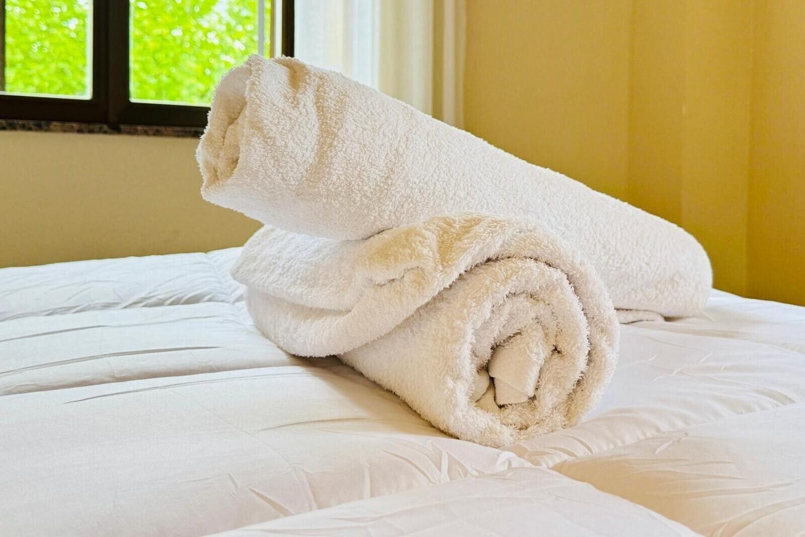 Cama con sábanas blancas y dos toallas enrolladas.